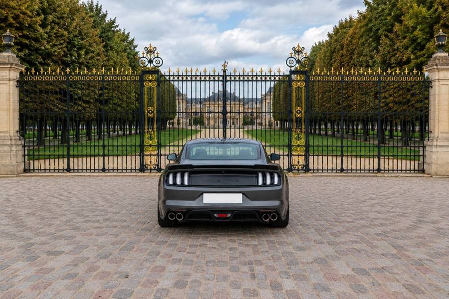 Ford Mustang GT grise, vue arrière devant une grille dorée